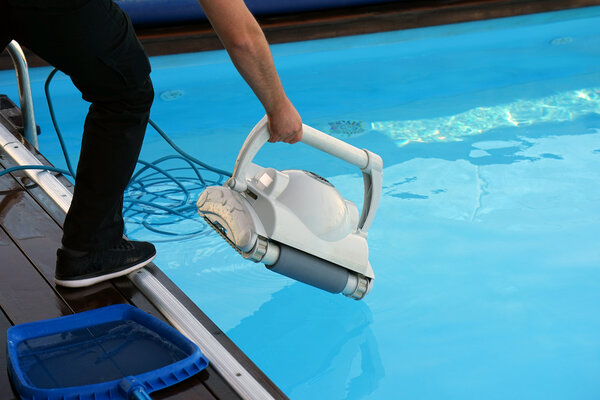 Eine Person nutzt einen Roboter-Poolreiniger, um den Pool zu reinigen, mit klarem Wasser und einer blauen Poolabdeckung.